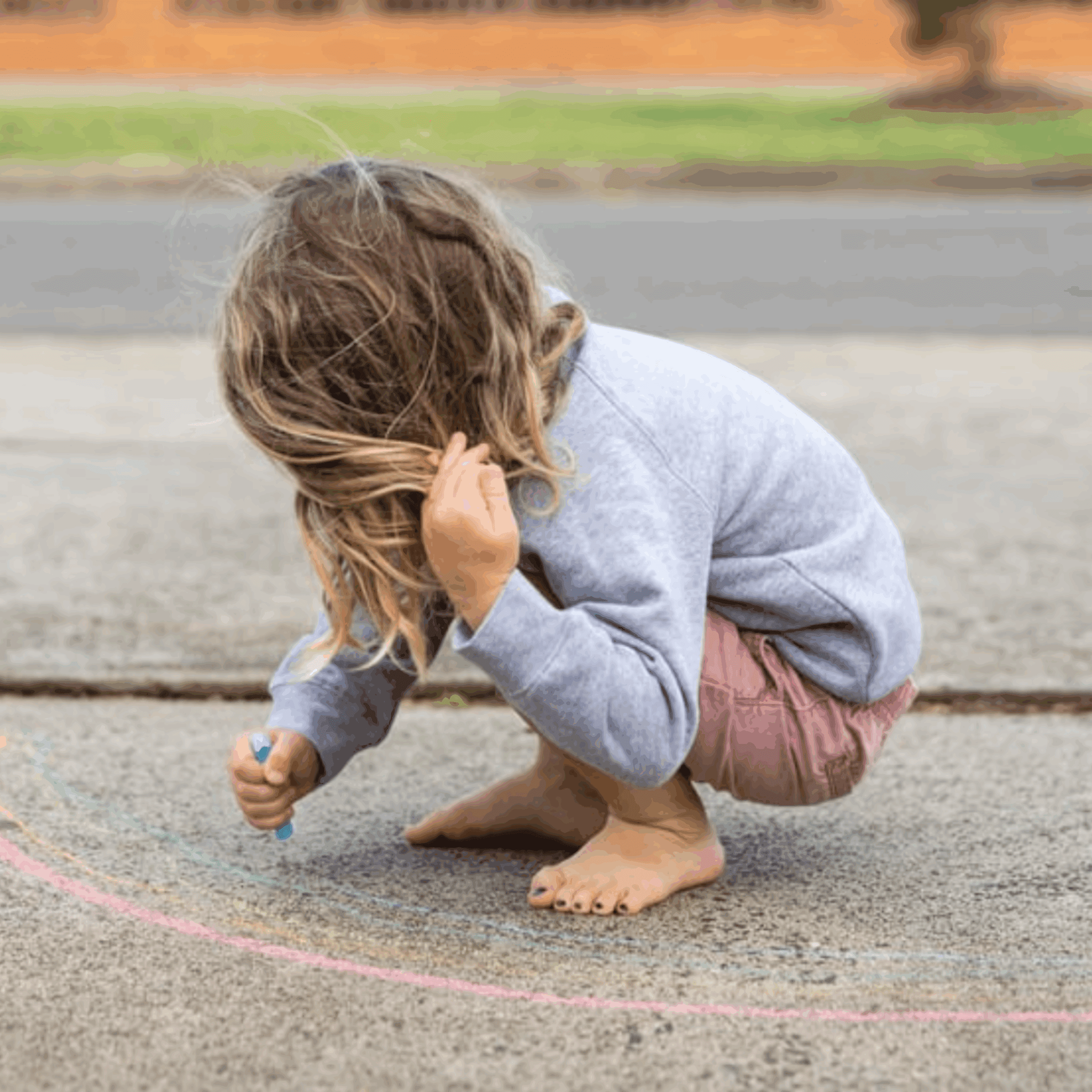 child with long hair covering face drawing on the side walk